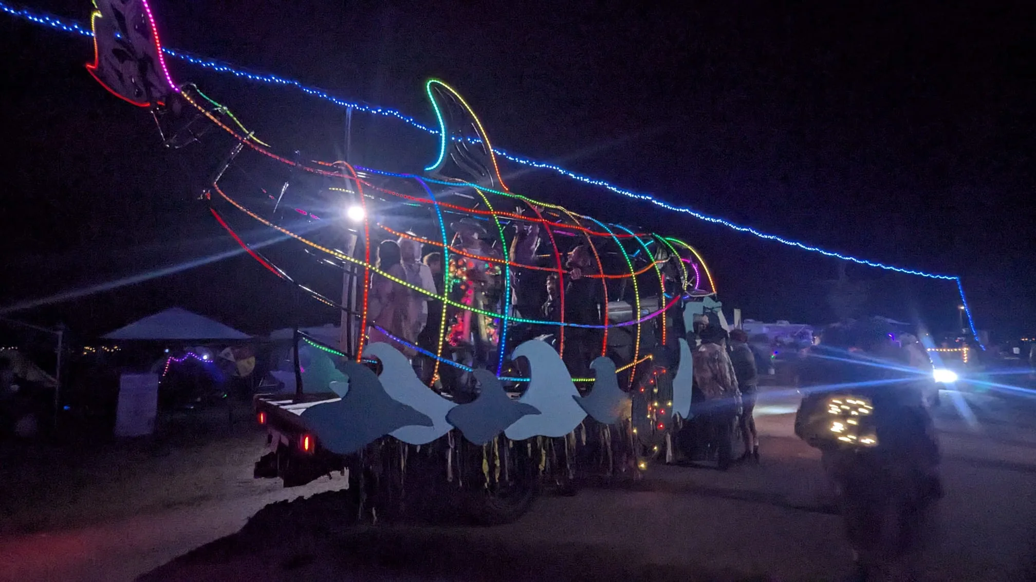 The Orcar lit in rainbow LEDs moving through the festival grounds at night with passengers inside