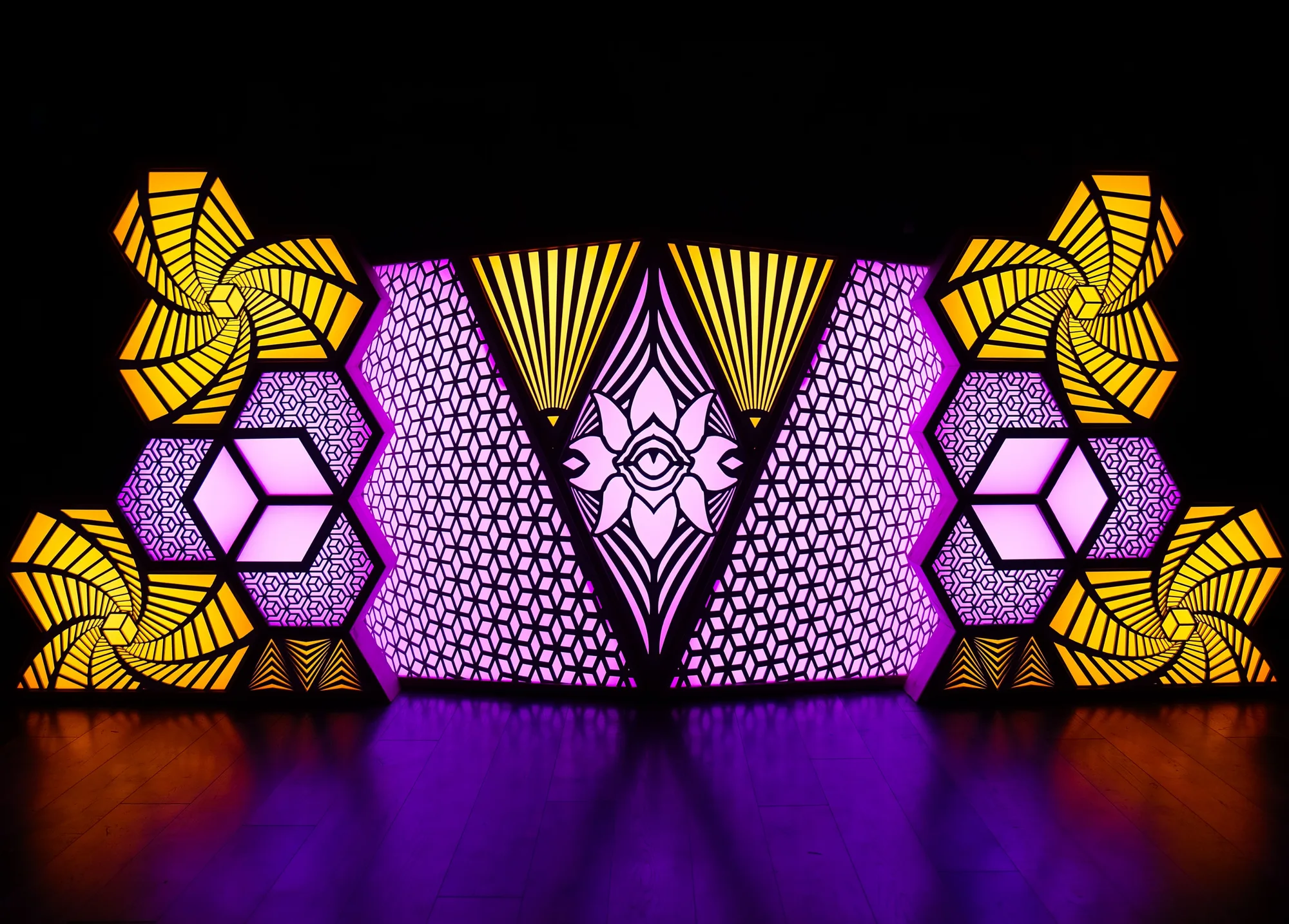 The Observer lit in purple and gold: laser-cut hexagon cubes and spiral panels either side of a central lotus with an eye, reflected on a dark floor