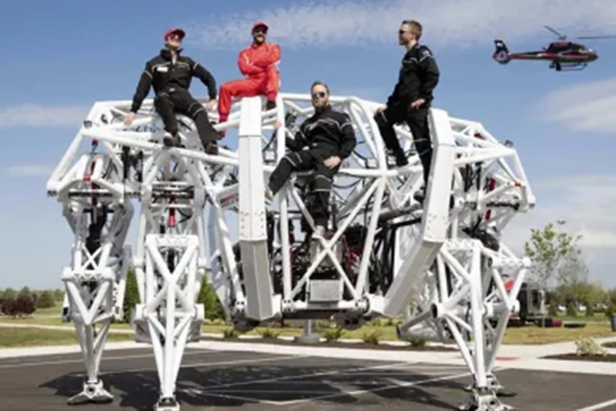 Four people sitting on top of Prosthesis, showing the scale of the mech