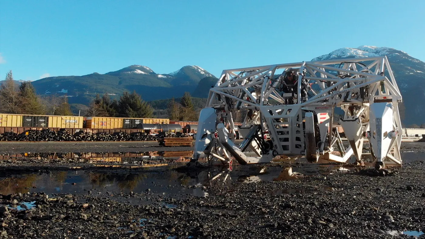 Prosthesis walking across a gravel yard in Squamish with snow-capped mountains behind
