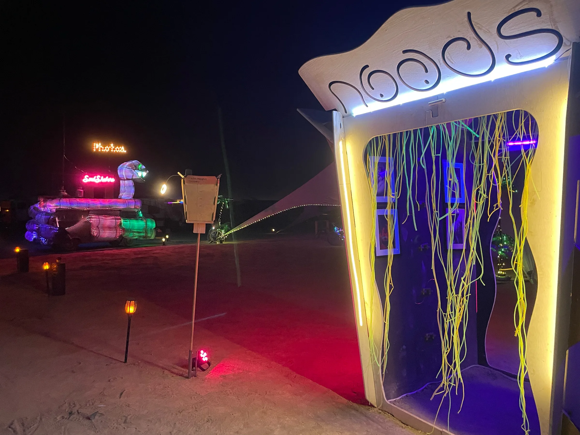 The Noodle Box at night, its NOODS lid lit gold and a curtain of glowing green noodle strands hanging across the open front