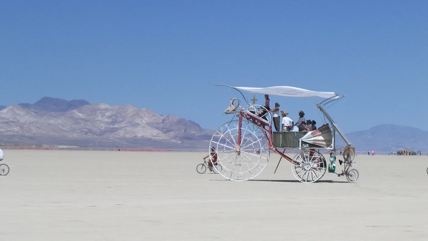 Daisy crossing the open desert playa by day with passengers under its solar canopy