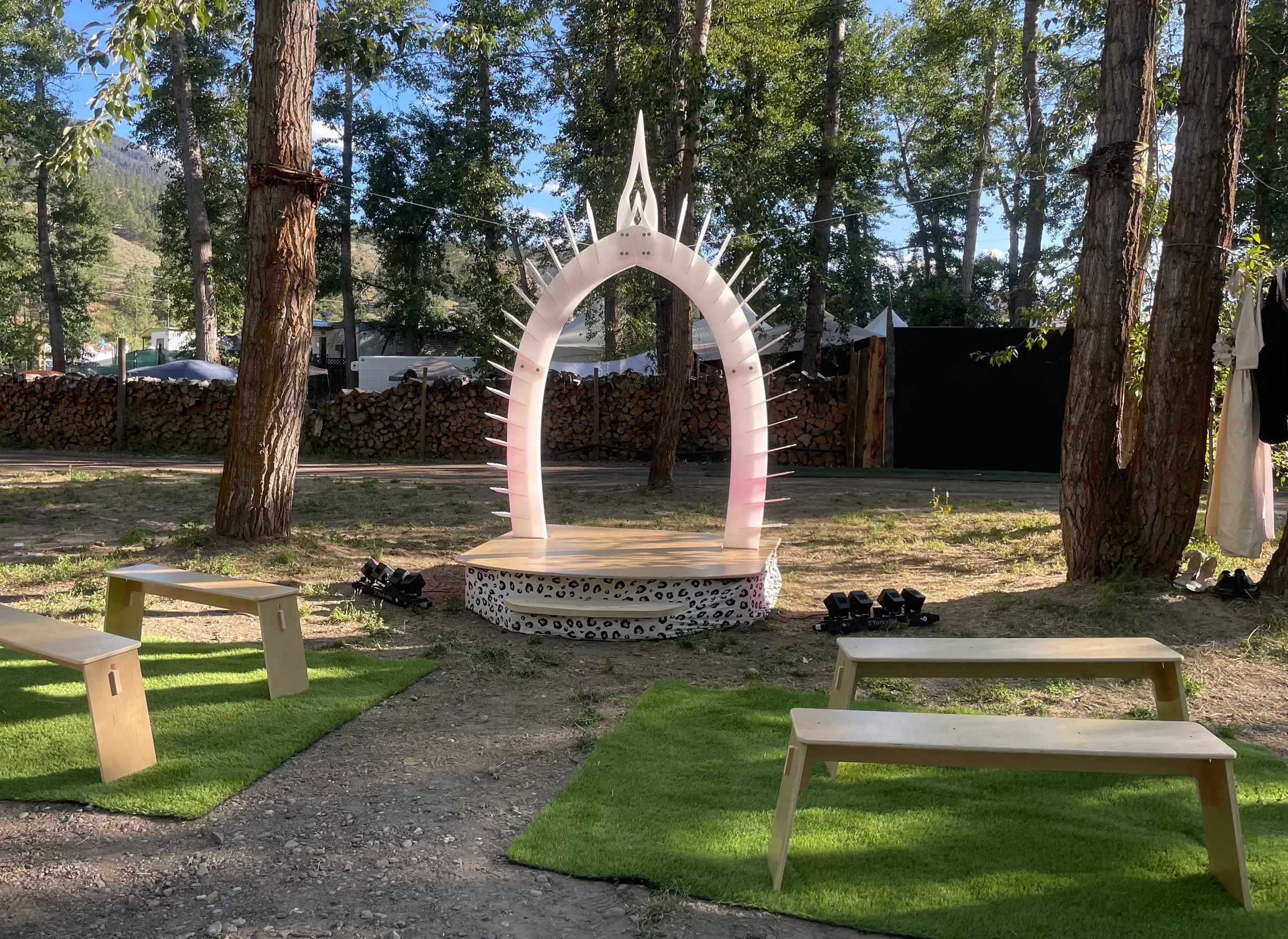 The Arch by day on its round platform in a forest clearing, with benches set out on turf for guests