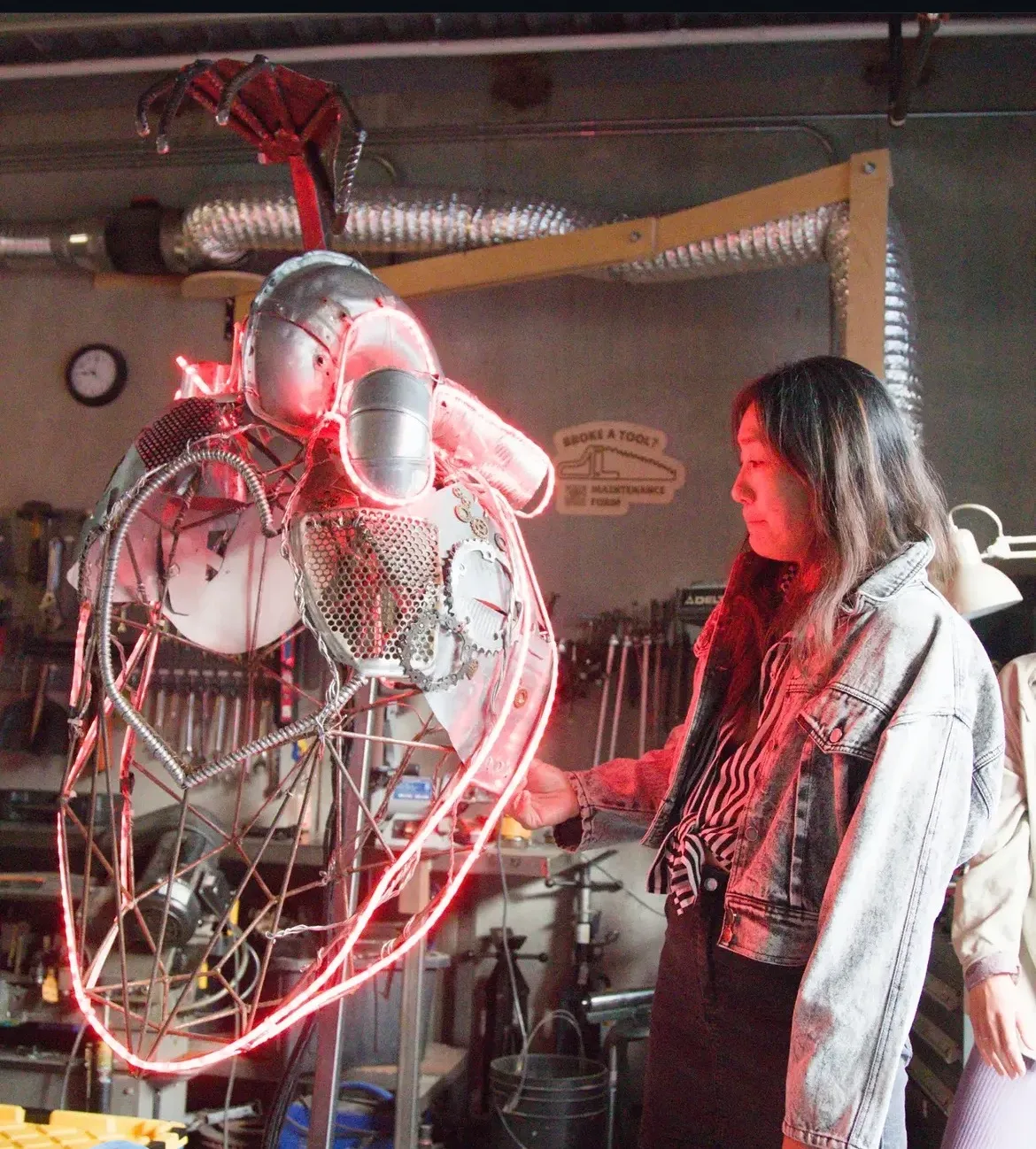 Lead artist Tif! Shen beside the HeART Pod in the workshop: a suspended metal anatomical heart outlined in glowing red light